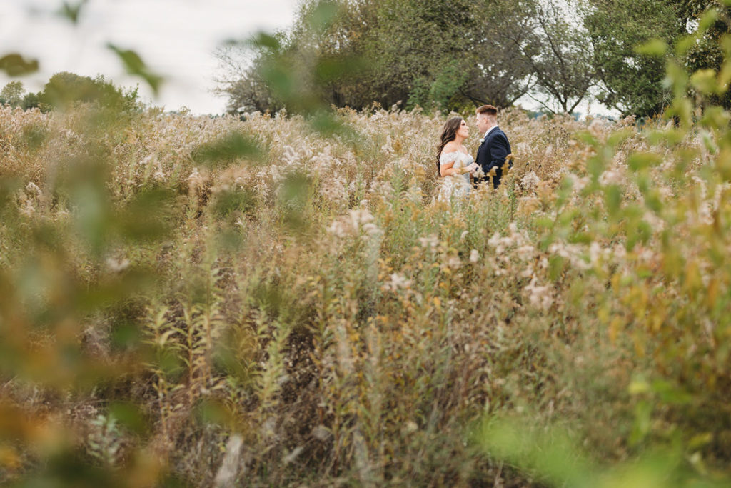 wide shot of bride and groom in the middle of a meadow with tall plants and grass around them during their white willow farms wedding