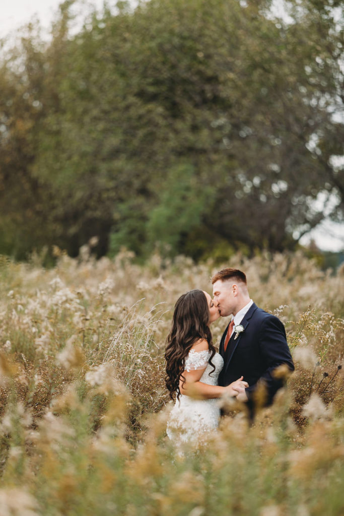 wide shot of bride and groom kissing in the middle of a meadow during their white willow farms wedding