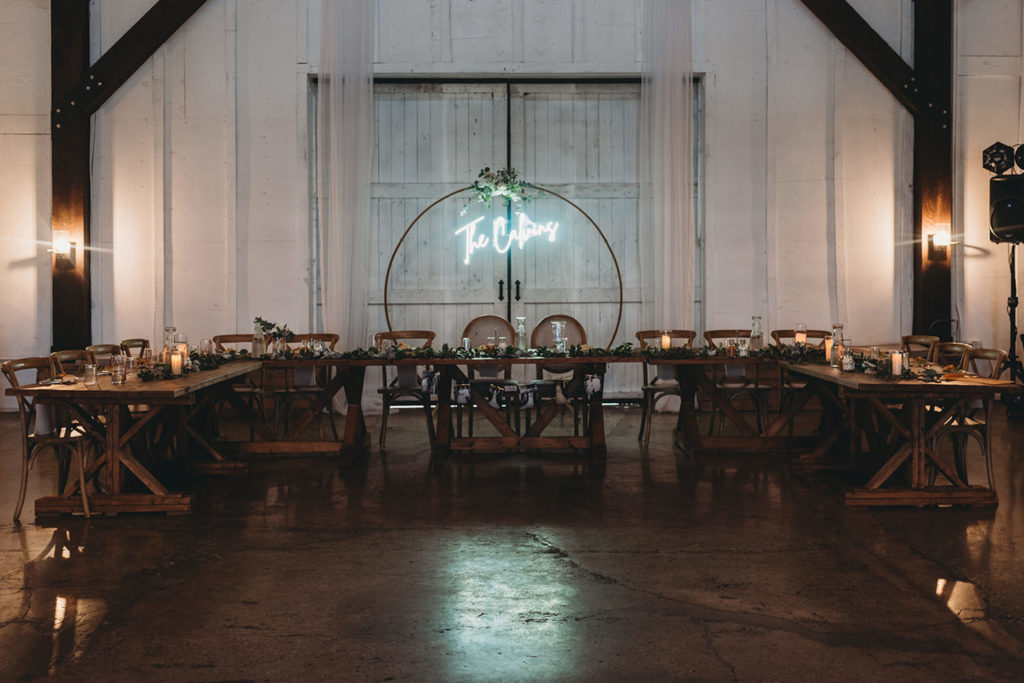 head table in u shape with wooden circle standing upright with neon sign hanging from it with the bride and groom's last name during their white willow farms wedding