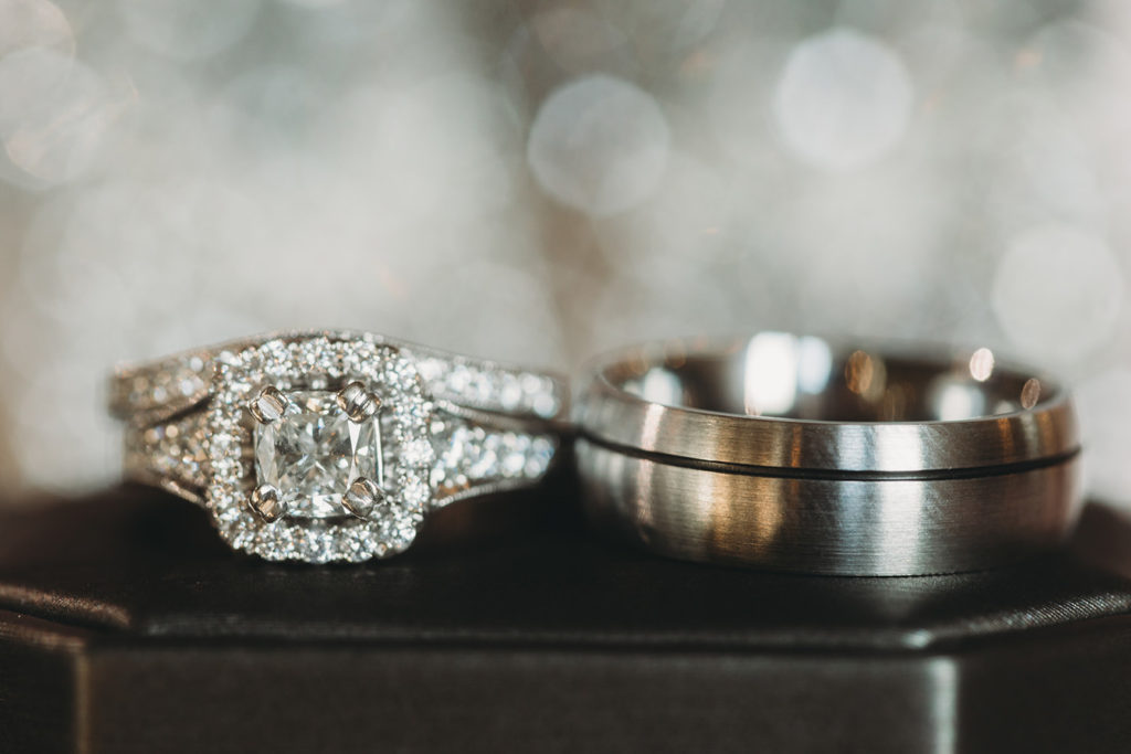 wedding band and engagement ring sit side by side with sparkly bokeh behind during their white willow farms wedding