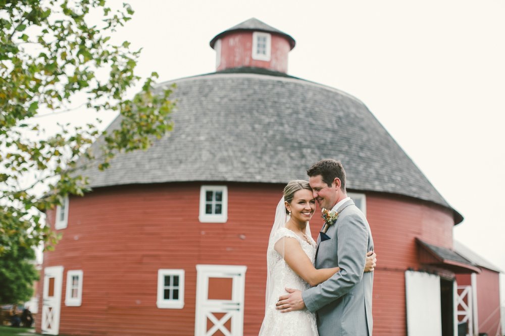 circular barn at kelley agricultural historical museum with bride and groom hugging in front is one of the Best Indianapolis Barn Venues