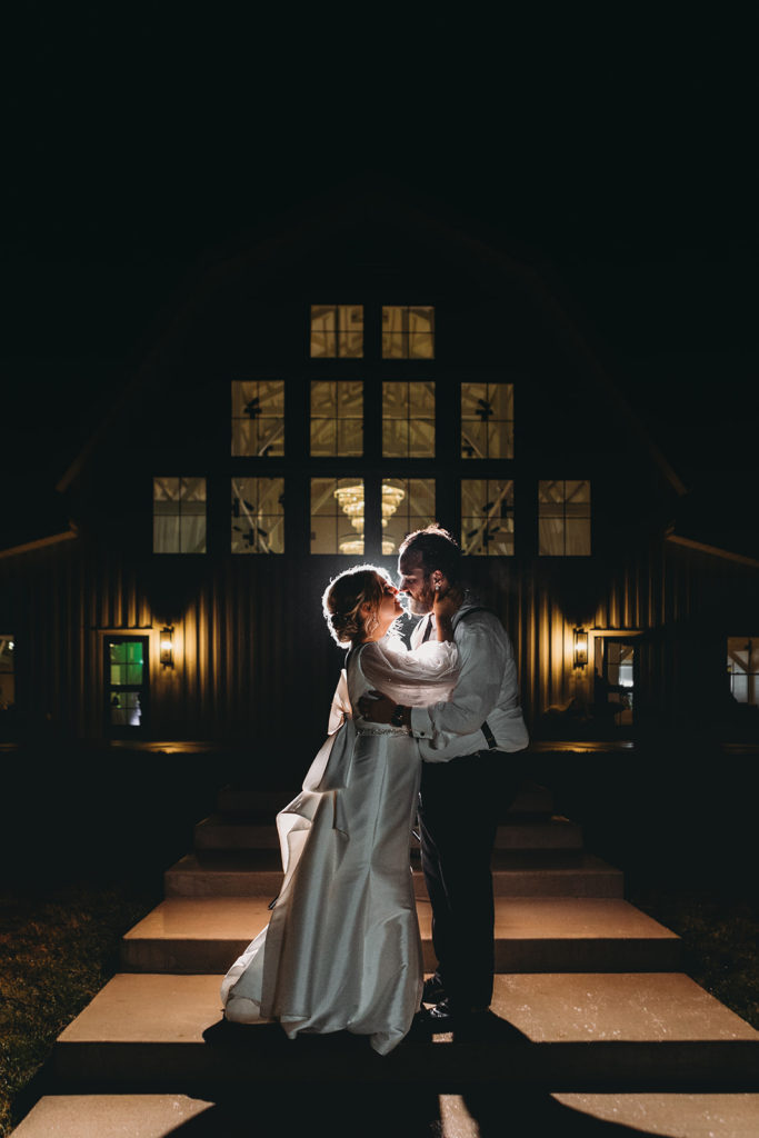 Bride and groom hold each other in front Sixpence at night all lit up.