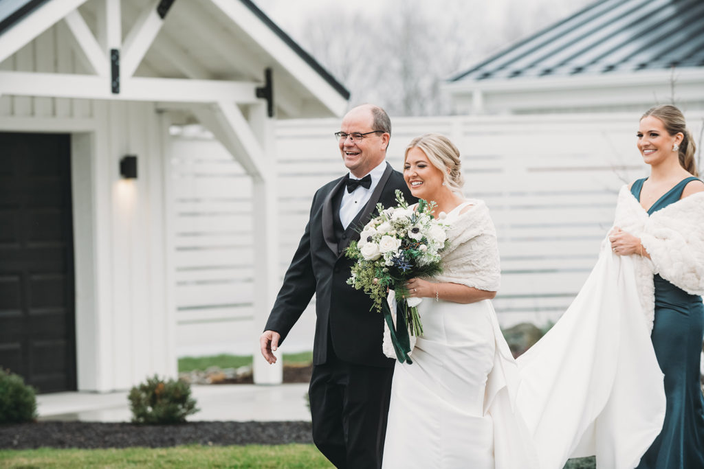 Bride walks down the aisle with father with smiles on their faces.