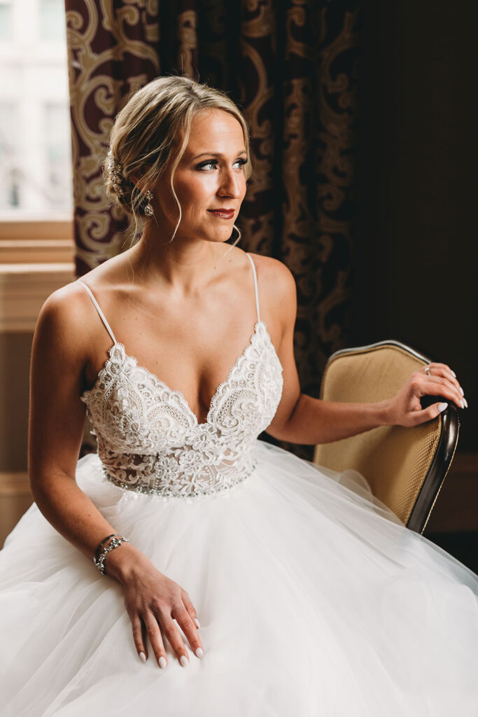 bride in wedding dress sitting on old chair looking out the window for a Union Station Indy Wedding