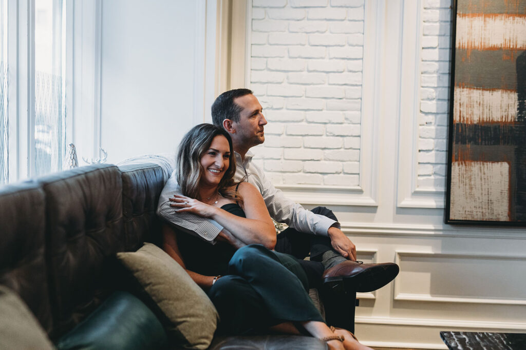 man and woman snuggle on couch in window light during their le meridien engagement photo session